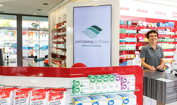 Eine Apothekerin der Petriesberg Apotheke steht hinter dem Tresen, im Hintergrund stehen ein Medikamentenregale.