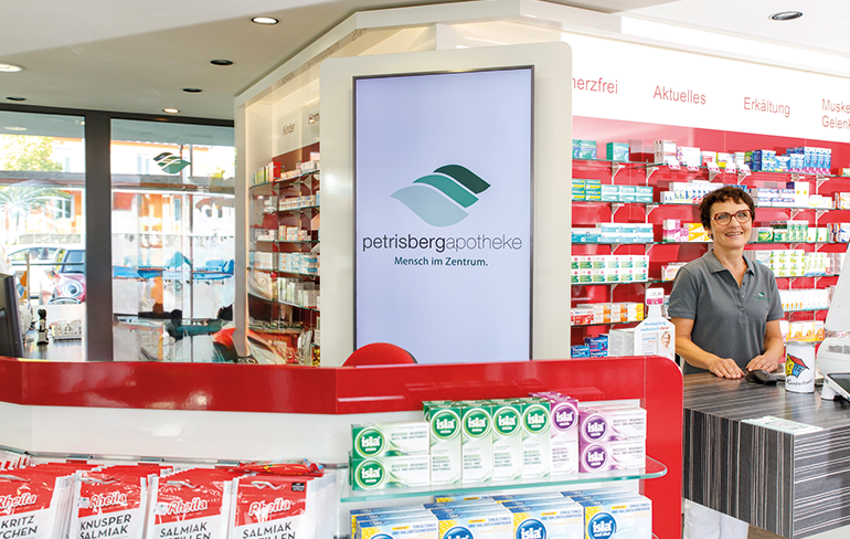 Eine Apothekerin der Petriesberg Apotheke steht hinter dem Tresen, im Hintergrund stehen ein Medikamentenregale.