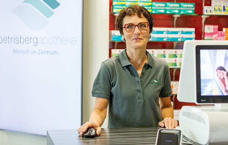 Eine Apothekerin der Petrisberg Apotheke in Trier steht hinter dem Tresen am Pc, dass unterstreicht die Fachkompetenz und technische Ausstattung der Apotheke.