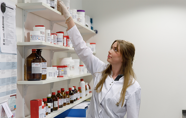 Eine Apothekerin der Petrisberg Apotheke steht im Labor vor einem Medikamentenregal und holt ein Flasche runter.