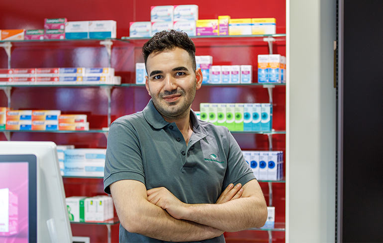 Der Inhaber der Petrisberg Apotheke steht vor dem Medikamentenregal und blickt in die Kamera.