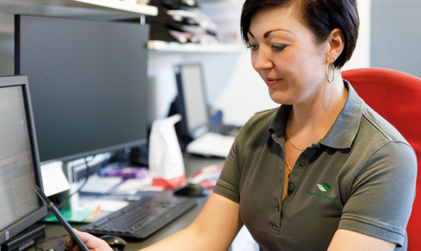 Apothekenmitarbeiterin sitzt im Büro an den PC´s, Sie hält ein Telefon in der Hand auf das Sie schaut.
